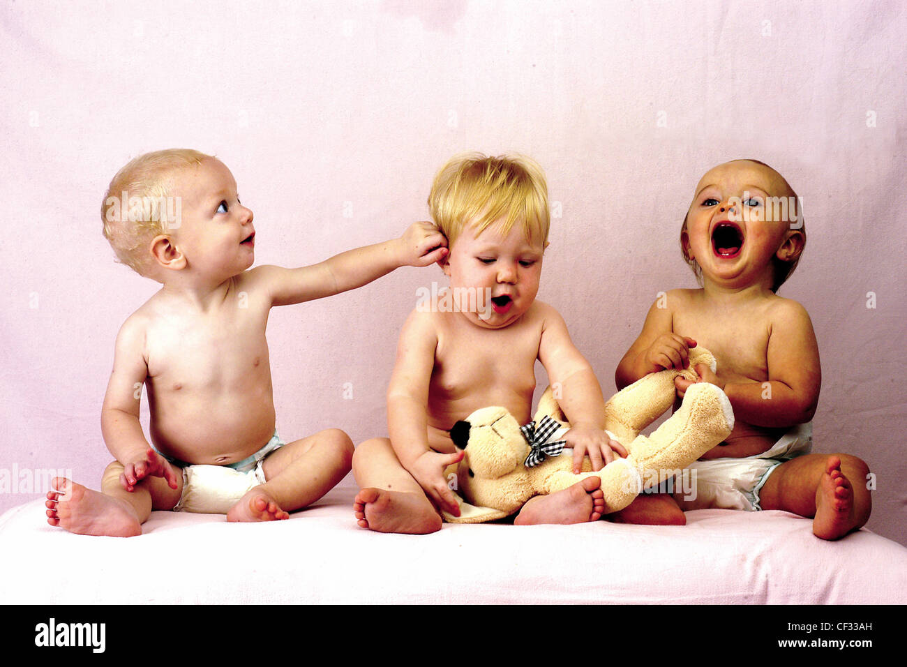 Tres bebés usando pañales, un bebé tocar otros en la cara, riendo, jugando  con un oso de peluche Fotografía de stock - Alamy