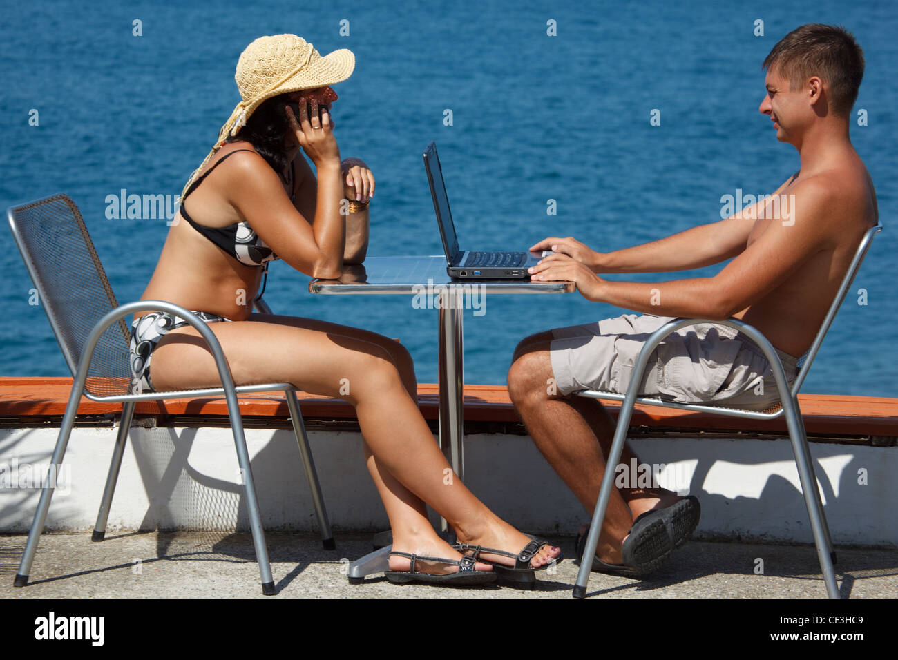 Un hombre y una mujer sentados en la mesa a cielo abierto en el fondo del mar. El hombre trabaja para el portátil. La chica que hablaba por teléfono. Foto de stock