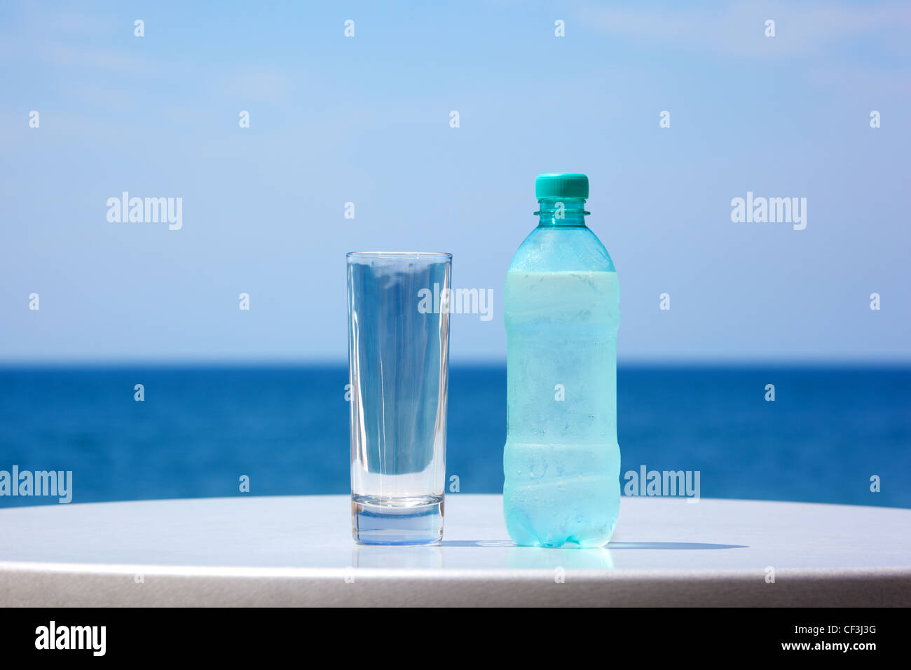 Botella de agua y cristal en la mesa bajo el cielo abierto en el fondo del mar. Foto de stock