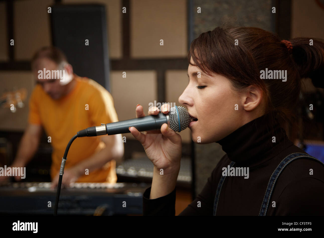 Chica vocalista canta en studio. tecladista en fuera de foco Foto de stock