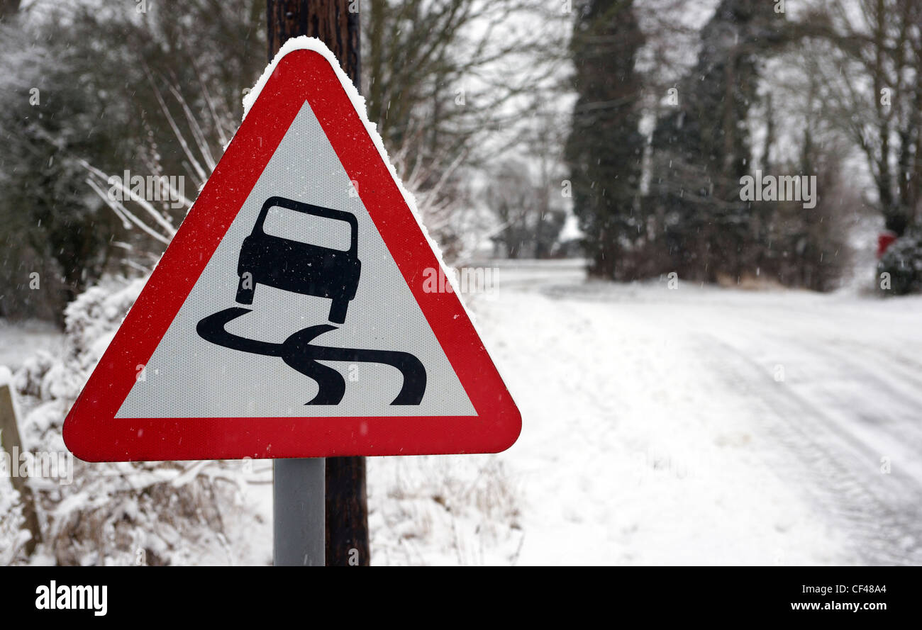 Una señal de carretera resbaladiza rural con un camino cubierto de nieve en el fondo, en Essex. Foto de stock