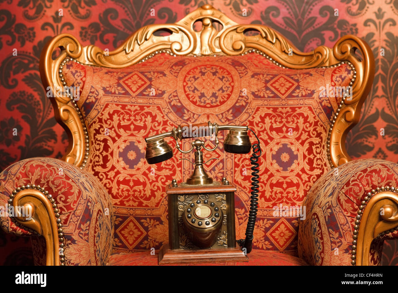 Teléfono antiguo es una silla roja con toques dorados, rojo vintage papel tapiz. Se centran en el teléfono Foto de stock