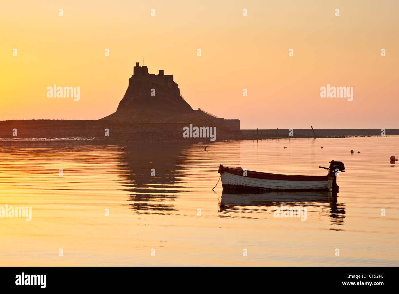 Un pequeño barco amarrado por el castillo de Lindisfarne al amanecer. Foto de stock