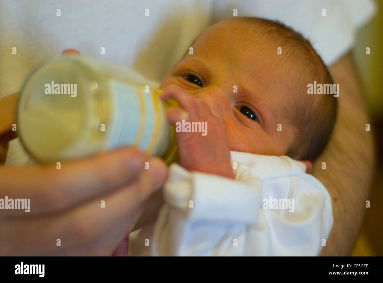 Un bebé recién nacido mujeres vestidas de blanco, babygrow retenidos por un  macho adulto alimentados con un biberón de leche Fotografía de stock - Alamy