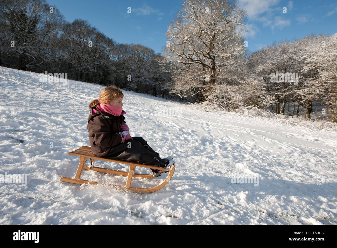Una niña bajando una pendiente cubierta de nieve en un trineo de ...