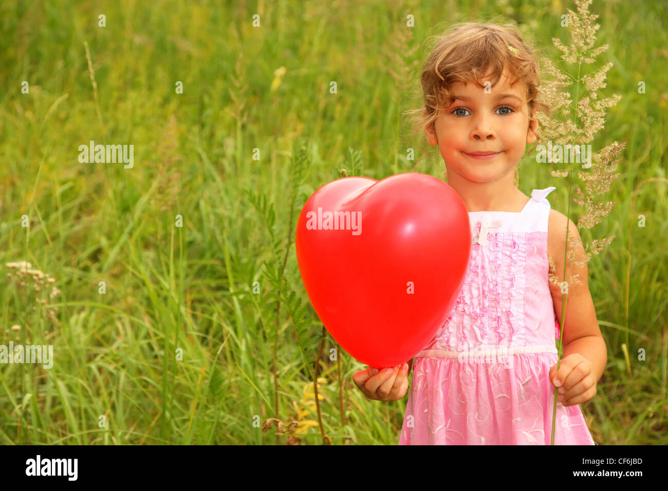 Hermosa niña vestido rosado celebración globo rojo. Chica en la naturaleza Foto de stock