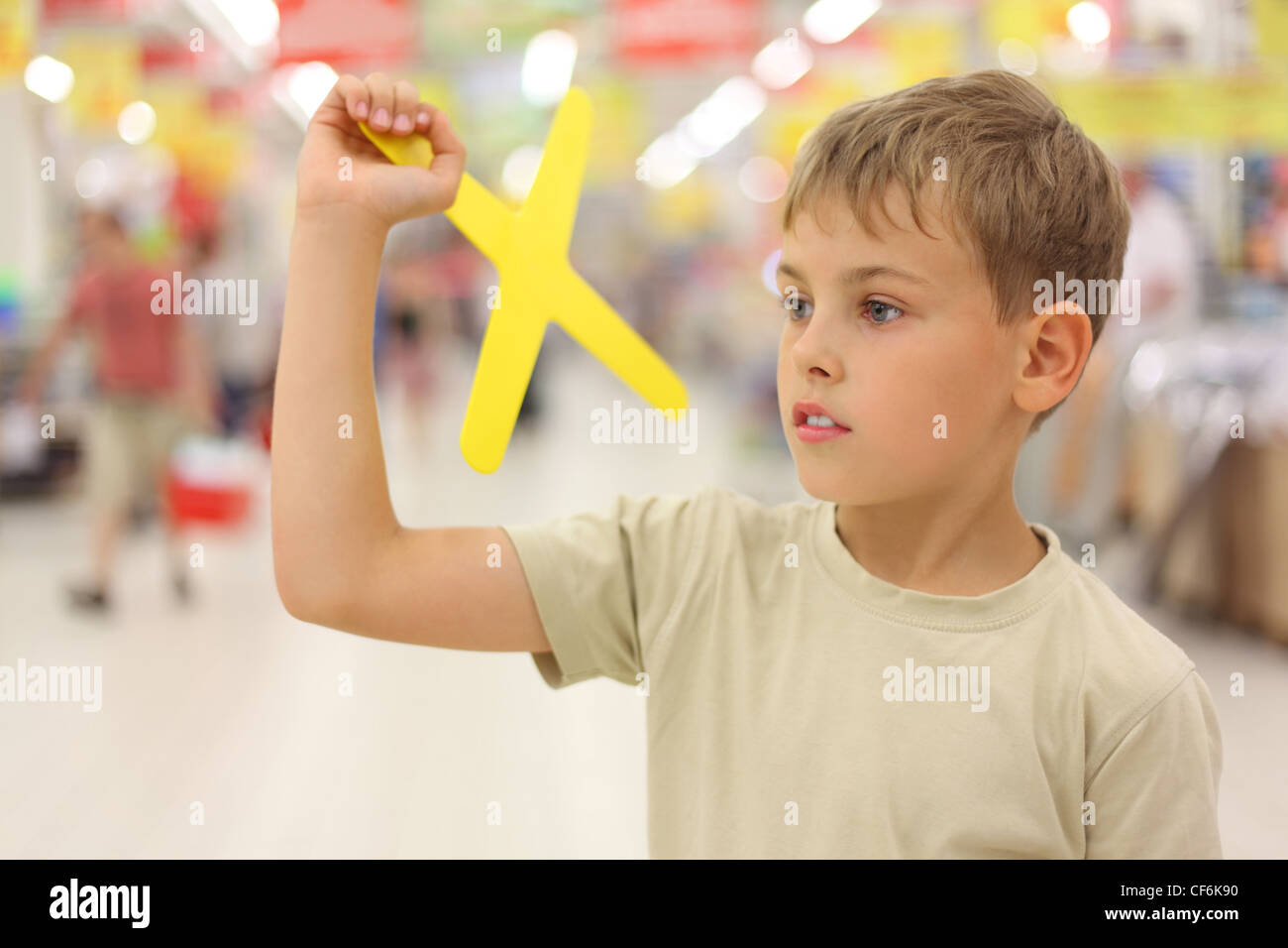 Poco caucásico niño sosteniendo amarillo boomerang toy, de pie en el gran  almacén, mirando a un lado Fotografía de stock - Alamy