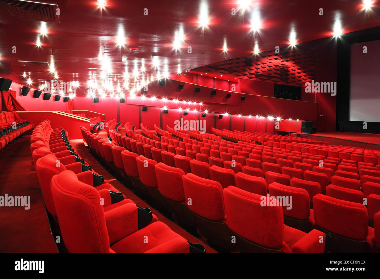 Filas de cómodas sillas rojas en iluminar la habitación roja cine Foto de stock