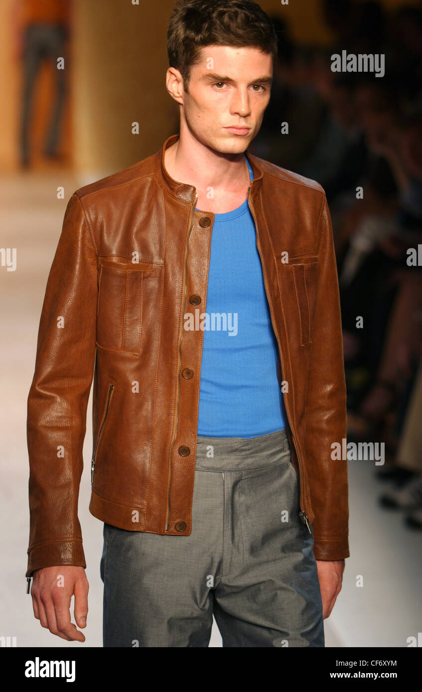 Calvin Klein Milán moda masculina S S hombres vestidos de chaqueta cuero marrón con cuello redondo camiseta azul sobre fondo borroso Fotografía de stock - Alamy