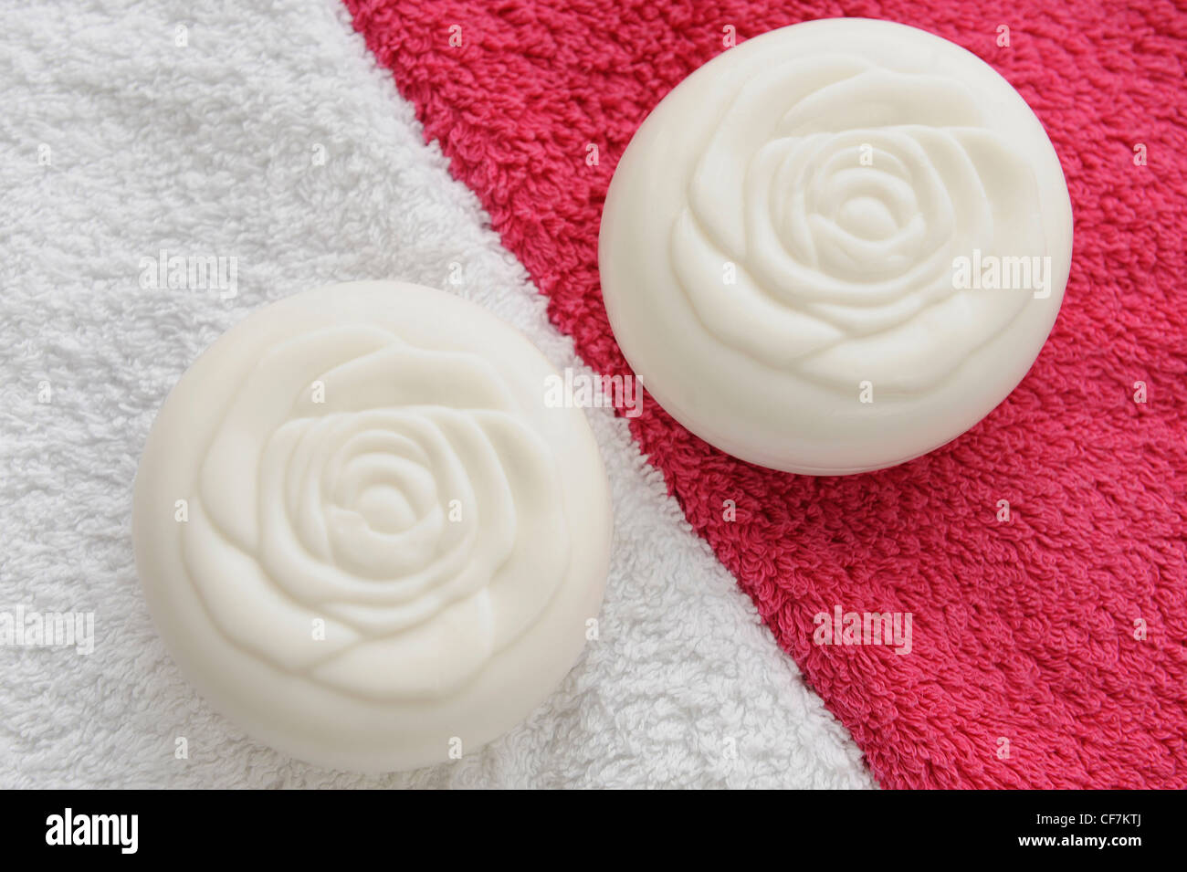 Dos barras de jabón redondo blanco un patrón en forma de rosa en la parte  superior de ellos, uno en una toalla blanca, el otro sobre una toalla rosa  brillante Fotografía de