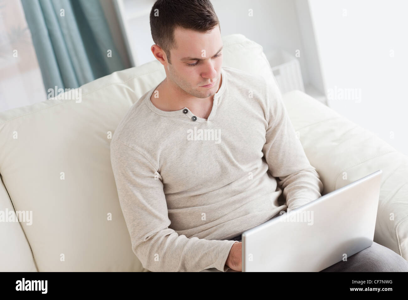Hombre con un portátil mientras está sentado en un sofá Foto de stock