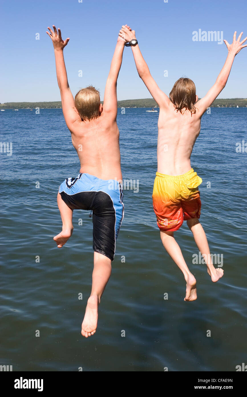 Dos niños (9 y 12 años de edad) saltando de dock en el lago, Sylvan Lake, Alberta, Canadá. Foto de stock