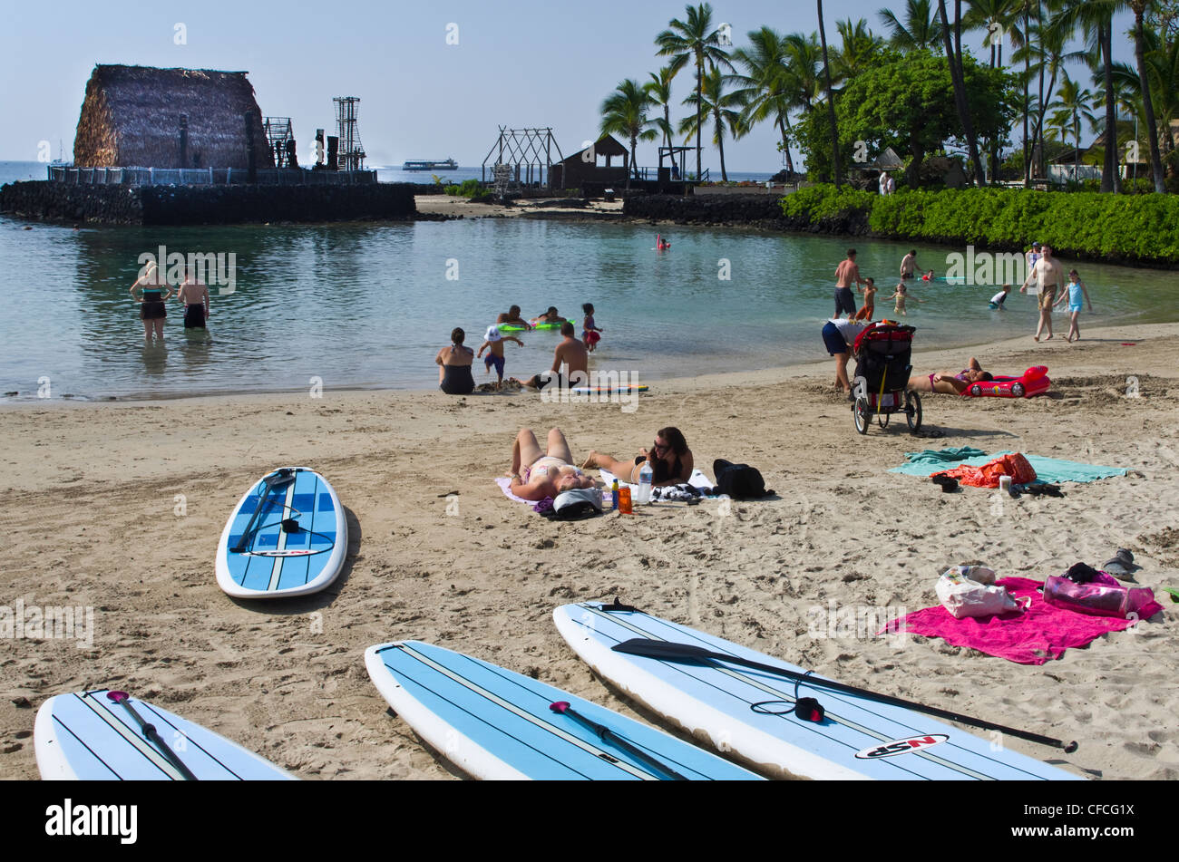 Paddleboards y bañistas en la playa Kamakahonu. "Ahu'ena Heiau en segundo plano. Foto de stock