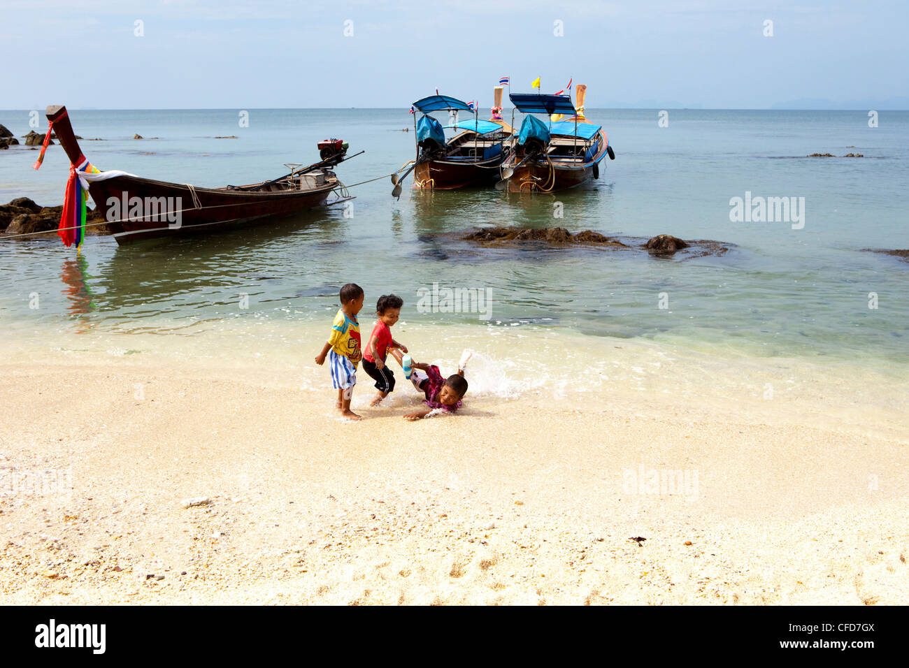 Los niños tailandeses jugando en la playa cerca de botes de cola larga, Koh Jum, Mar de Andaman, Tailandia Foto de stock