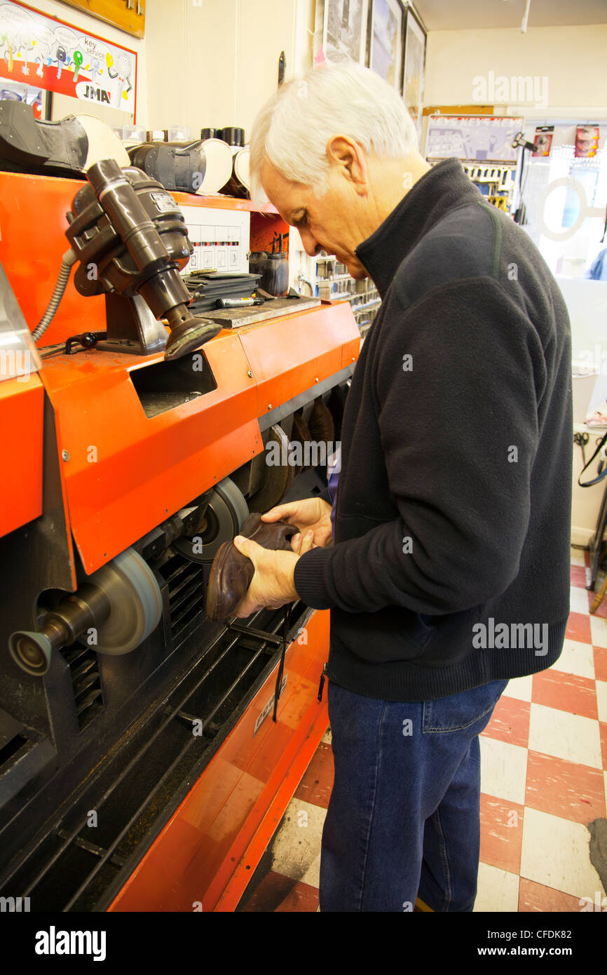 Zapato reparador arreglando zapatos en zapateros shop trabaja en la máquina para rectificar y pulir los zapatos Foto de stock