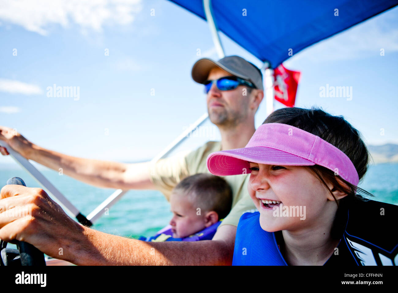 Un hombre pilotos un Pontoon Boat mientras su hijo de tres años ayuda a dirigir, y su hija de cinco años se sienta junto a ellos, el oso Lak Foto de stock