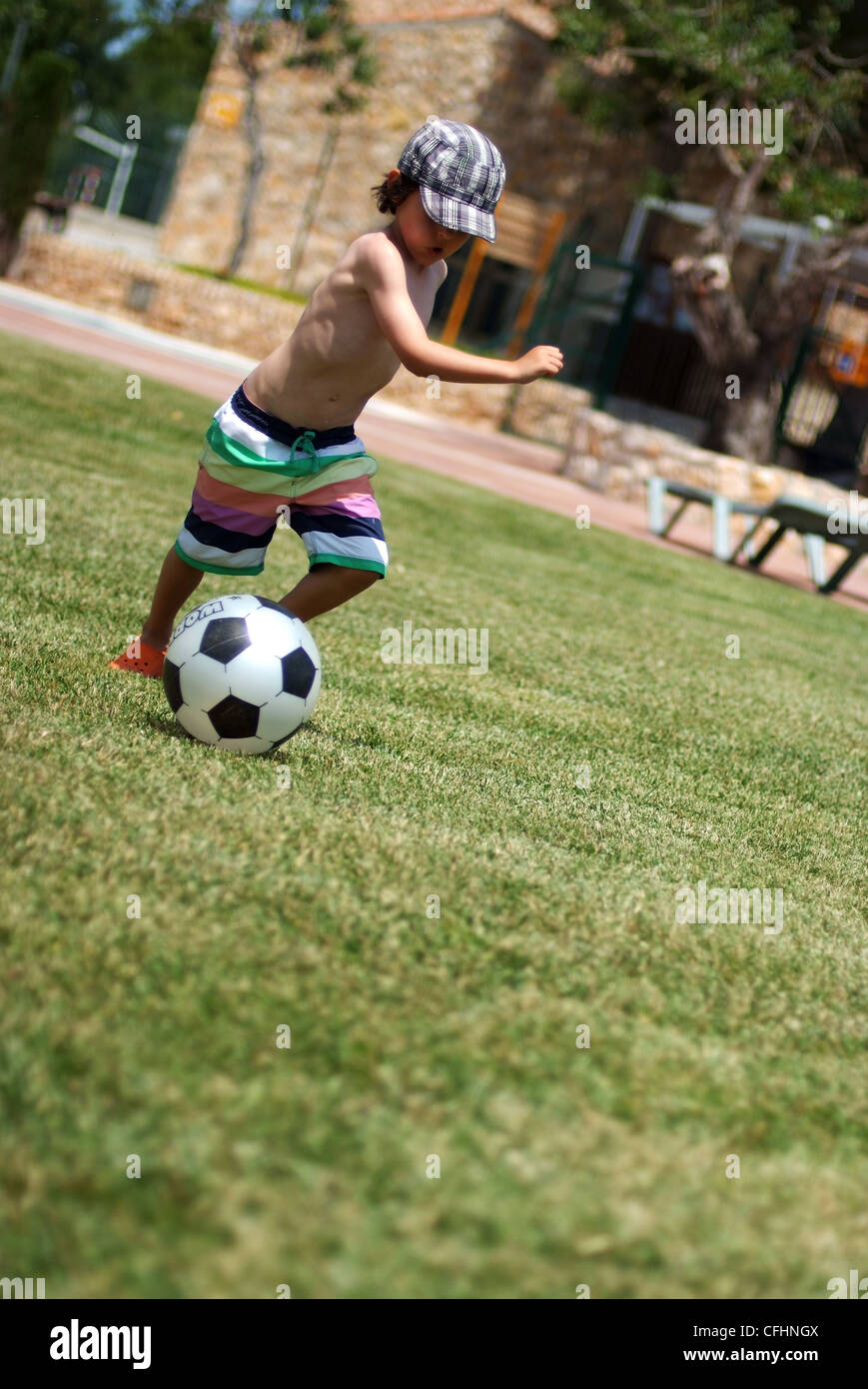Muchacho jugando al fútbol - un niño de cinco años se ejecuta con una pelota de fútbol en el césped en verano Foto de stock