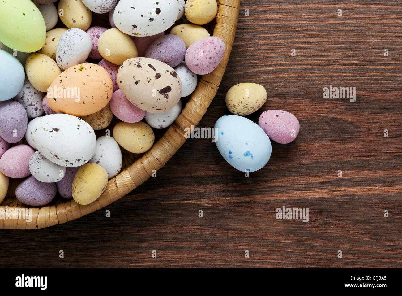 Todavía la vida foto de moteado cubierto de caramelo chocolate huevos de pascua en una cesta de mimbre sobre una tabla de madera rústica. Foto de stock