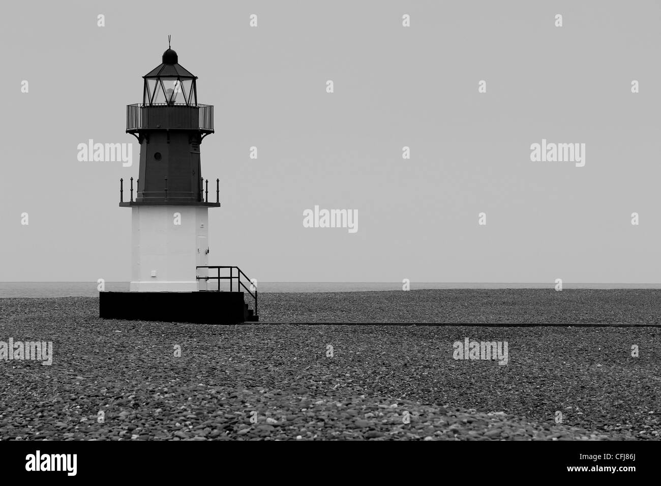 La imagen en blanco y negro de un faro sobre una playa de guijarros con marea baja. Foto de stock
