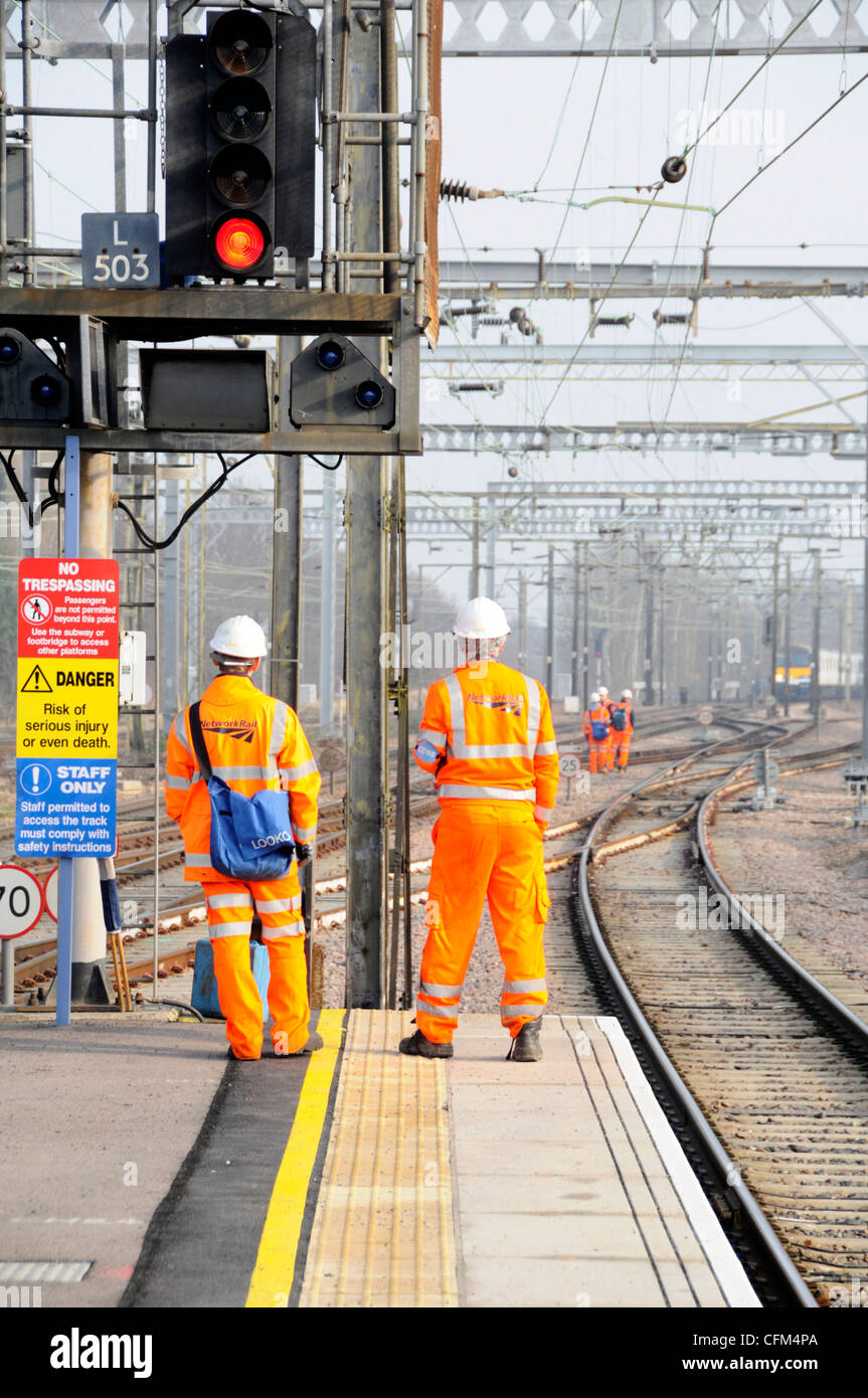 Vista posterior Network Rail Workmen en chaqueta de alta visibilidad & casco en la señal de ferrocarril signo grupo de trabajadores en Pistas más allá del tren de la distancia Essex Inglaterra Reino Unido Foto de stock