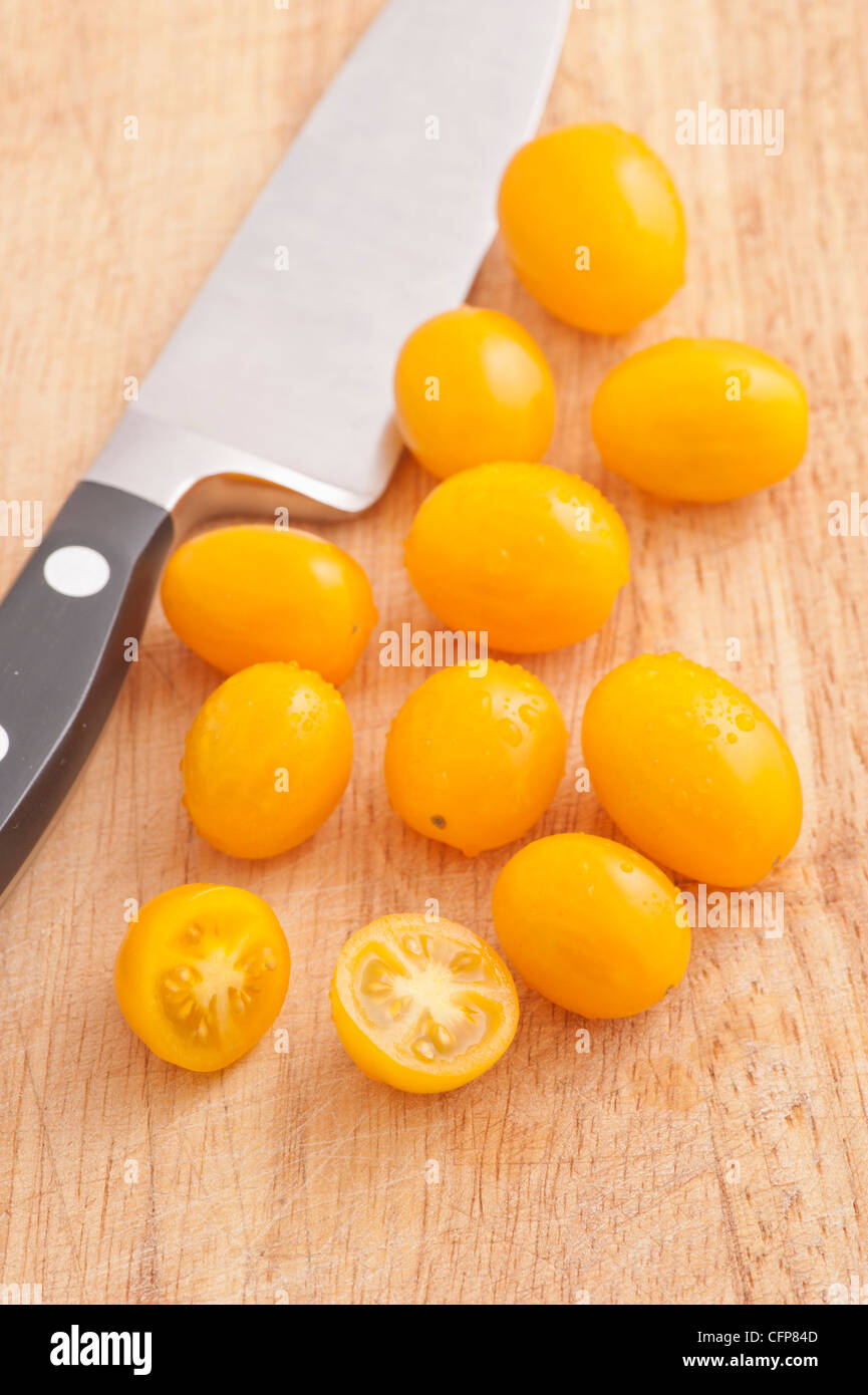 Tomates ciruela amarilla y un cuchillo de cocina sobre una tabla para cortar Foto de stock