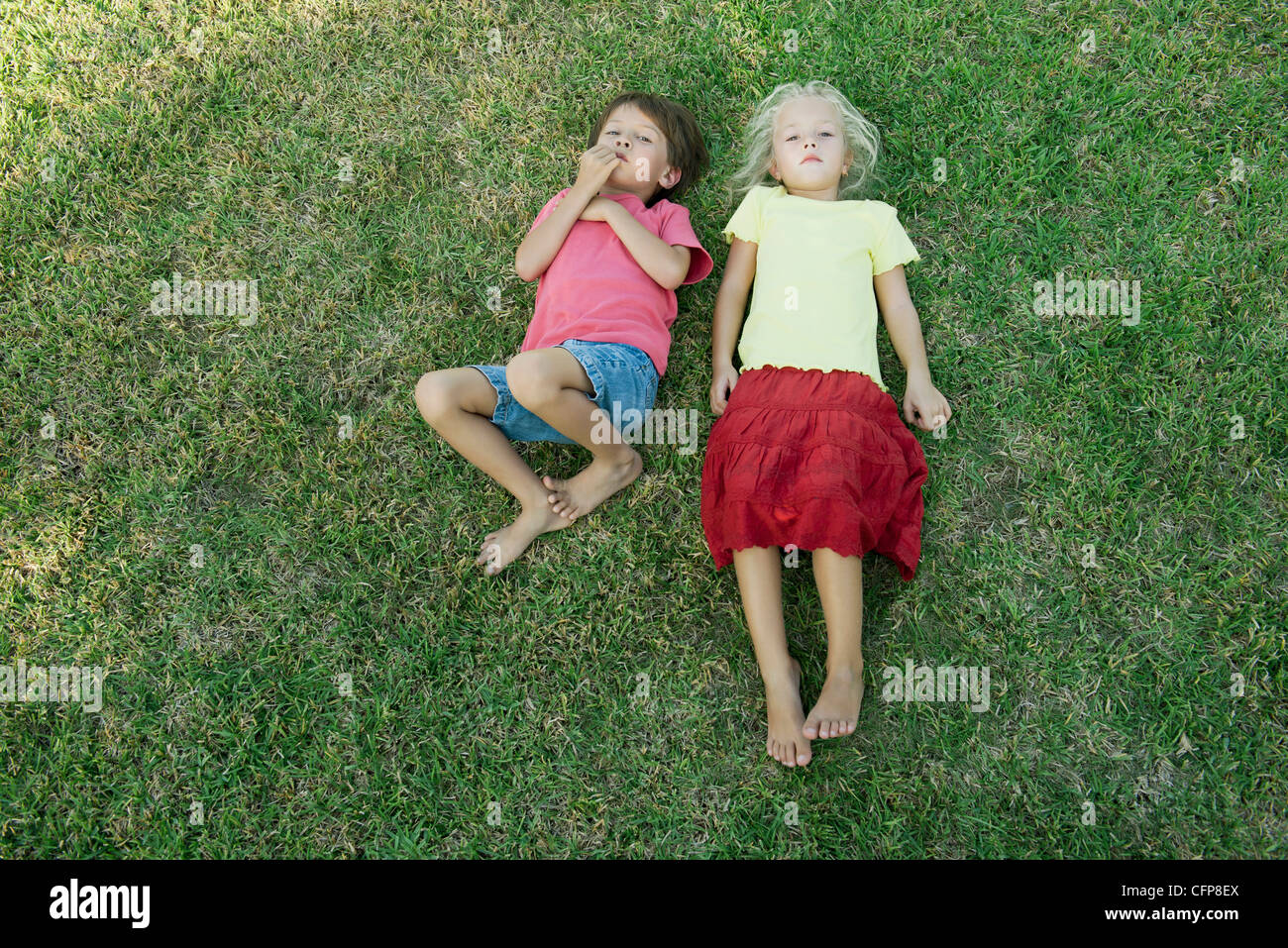 Los niños yaciendo juntos sobre el césped, mirando a la cámara Foto de stock