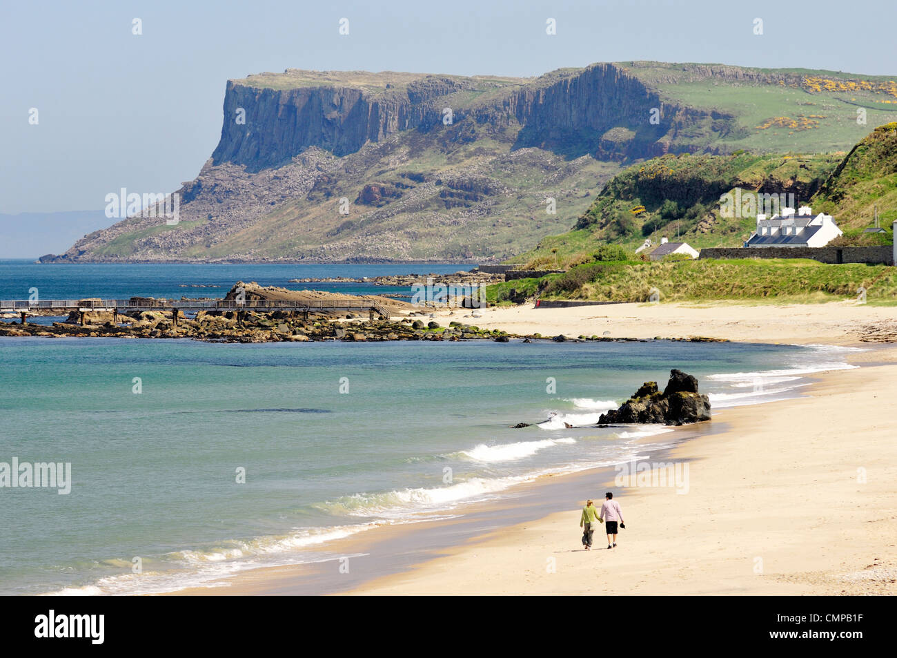 Pareja joven caminando en Ballycastle Beach, Condado de Antrim, Irlanda del Norte. Mirando hacia la cabecera de cabeza justo Foto de stock