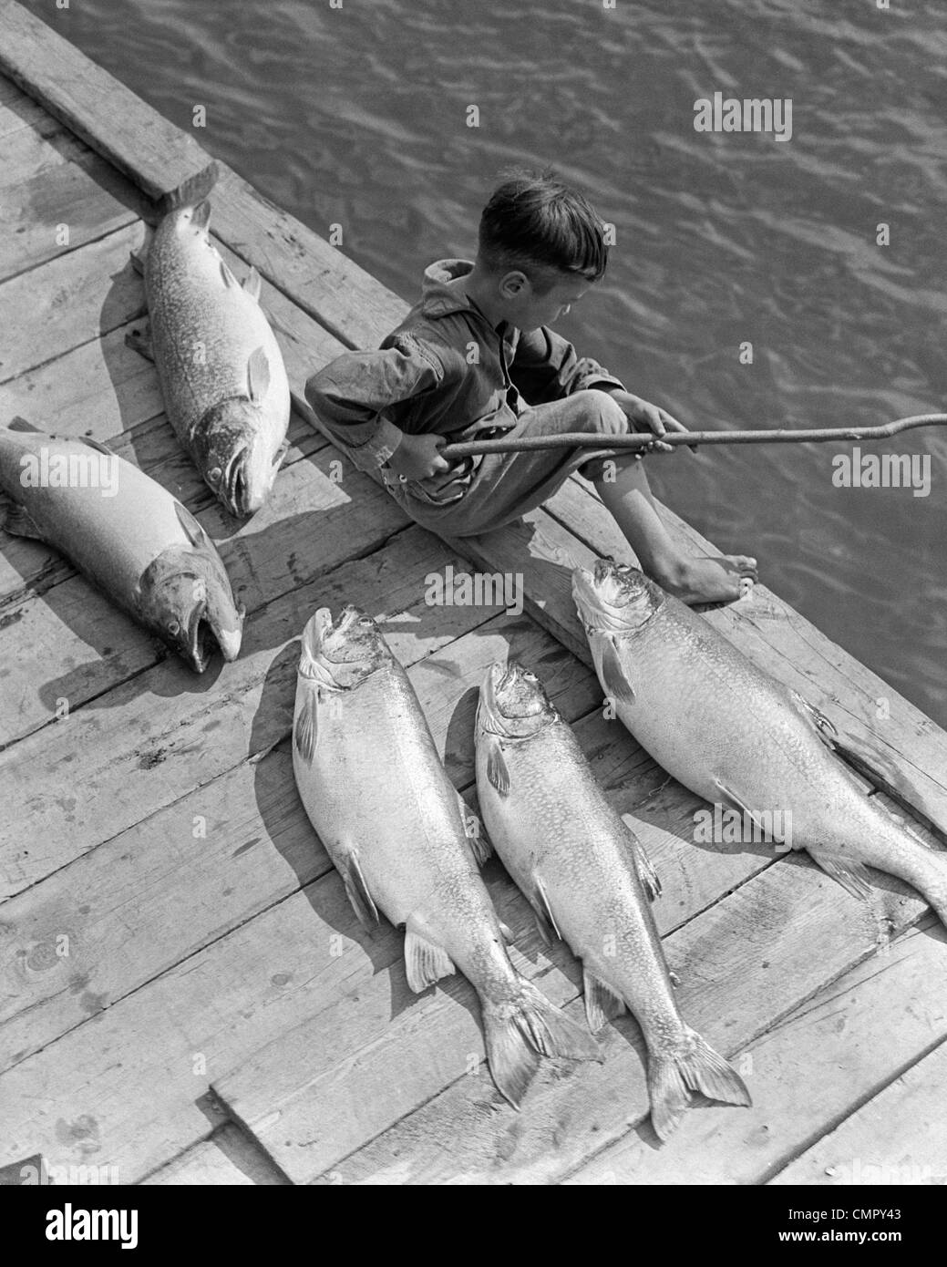 1930 chico sentado en el muelle con 5 grandes peces PESCA CON STICK POLE Foto de stock