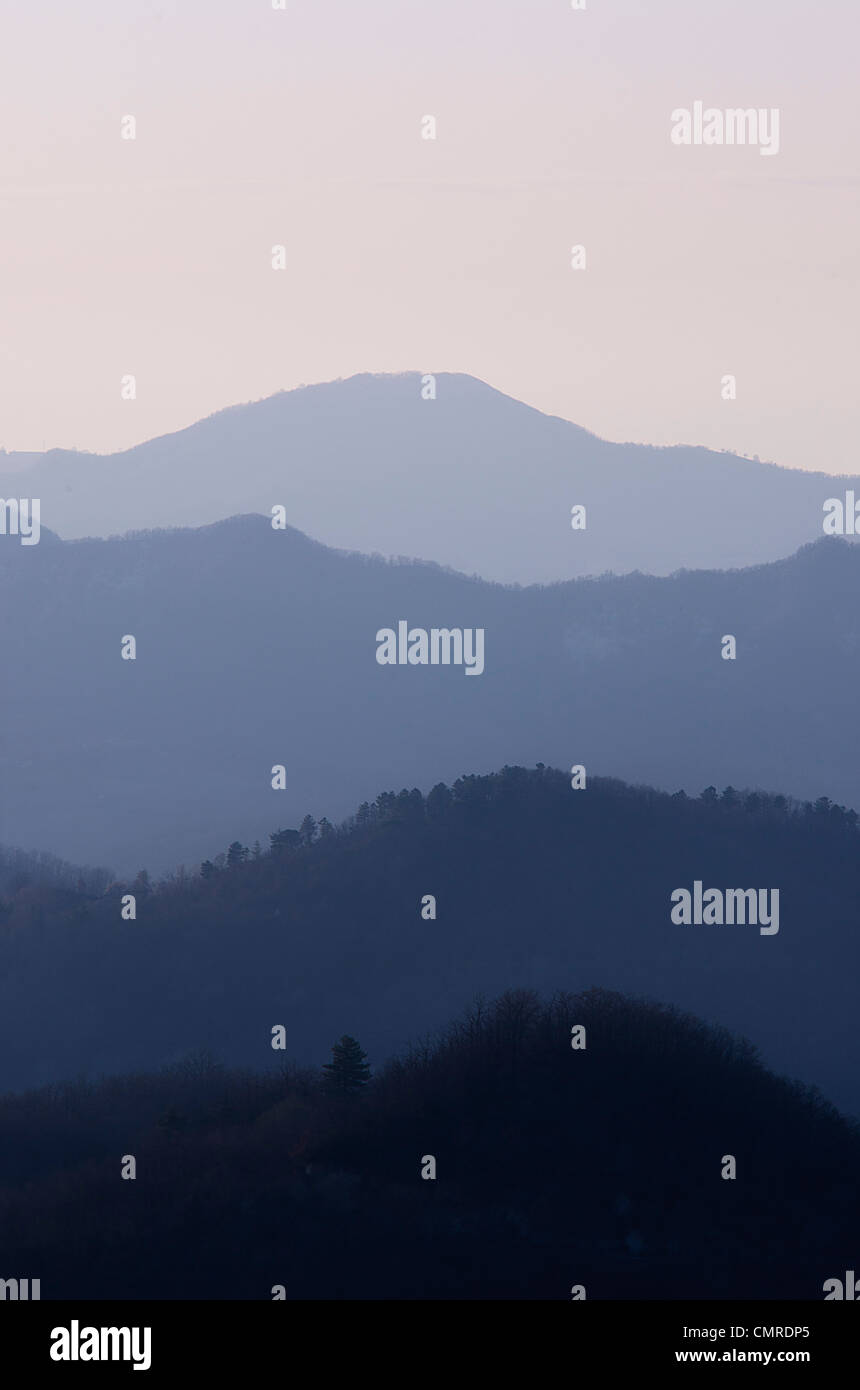 Vista del atardecer colinas suavemente degradantes del oscuro al claro azul en la niebla Foto de stock
