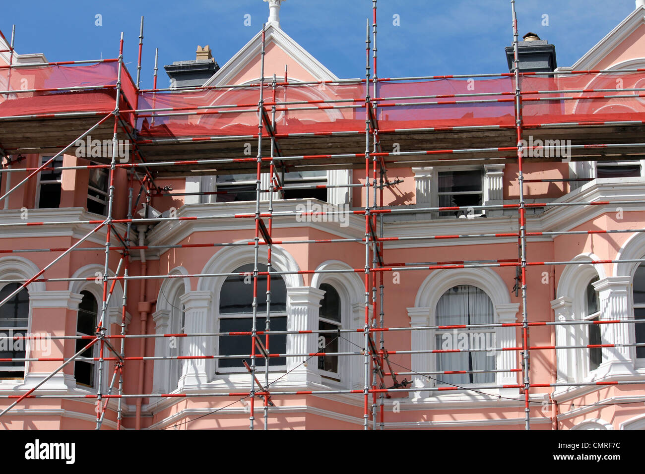 Andamios metálicos rojo contra una casa victoriana rosa y blanco contra un cielo azul Foto de stock