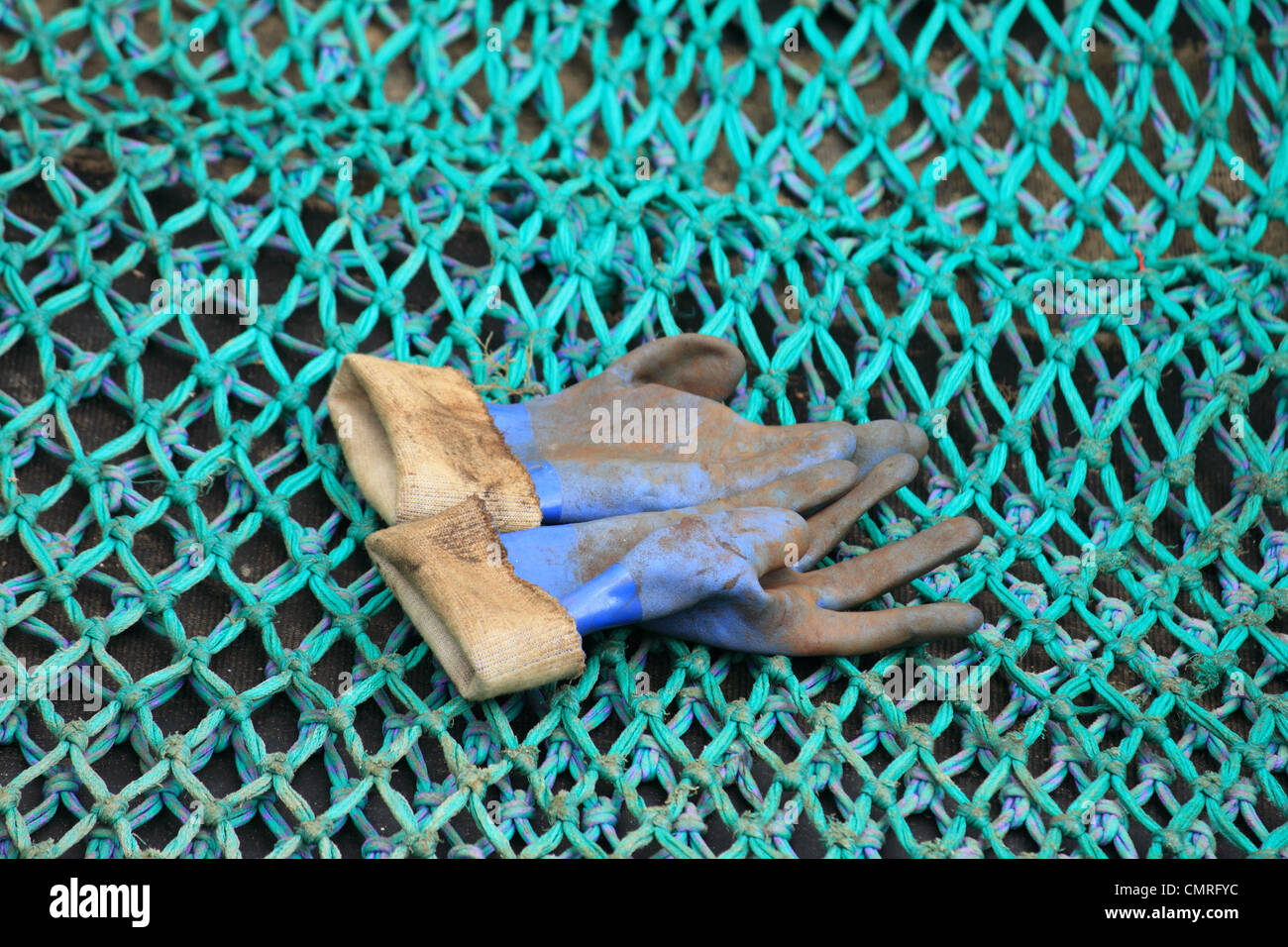 Pares de guantes de goma azul barro desechado en una gran red de pesca verde de malla Foto de stock