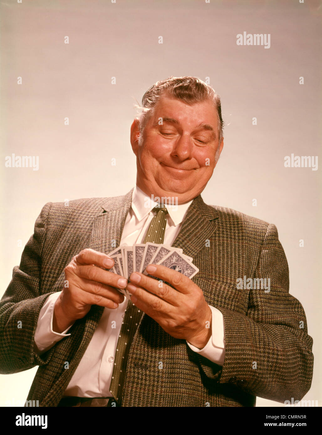 1960 1960 sonríe satisfecho hombre mirando las cartas mano repartida traje de negocios TIE JUEGO DE NAIPES APUESTAS POKER RETRO Foto de stock