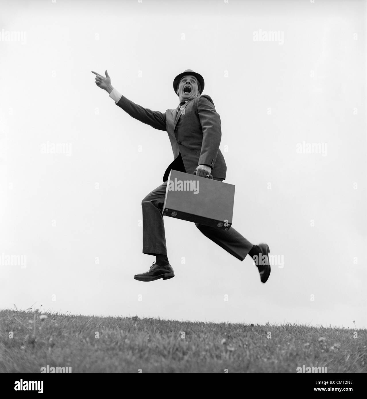 1960 El empresario con un maletín corriendo gritando y saltando EN EL AIRE EXTERIOR DEDO apuntando hacia adelante Foto de stock