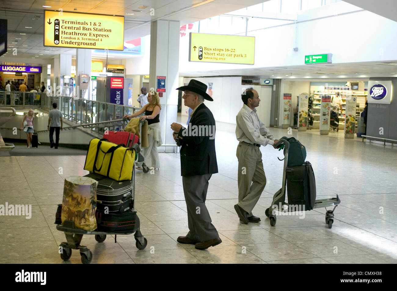 Pasajero con carrito de equipaje en el área de llegadas del aeropuerto de Heathrow Foto de stock