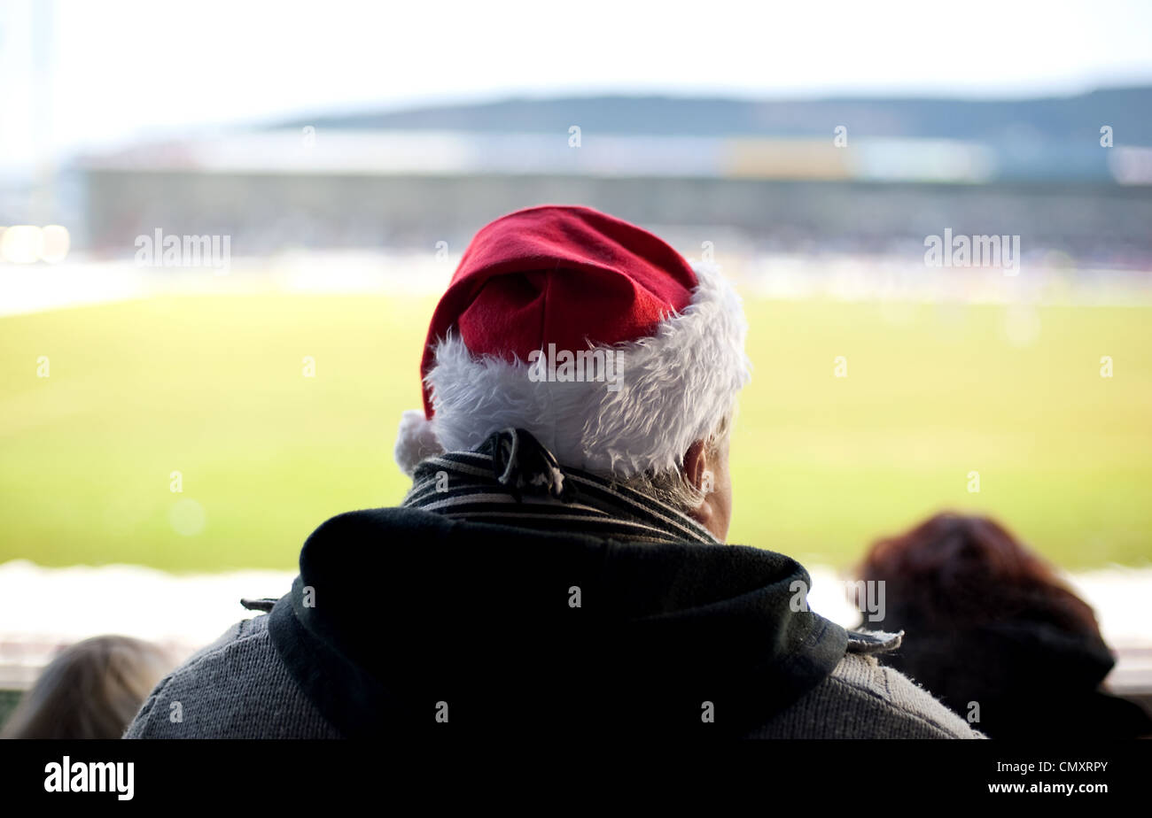 Un fanático del fútbol visto desde atrás en la multitud observa el juego en el tiempo de Navidad llevando un gorro de Papá Noel. Foto de stock