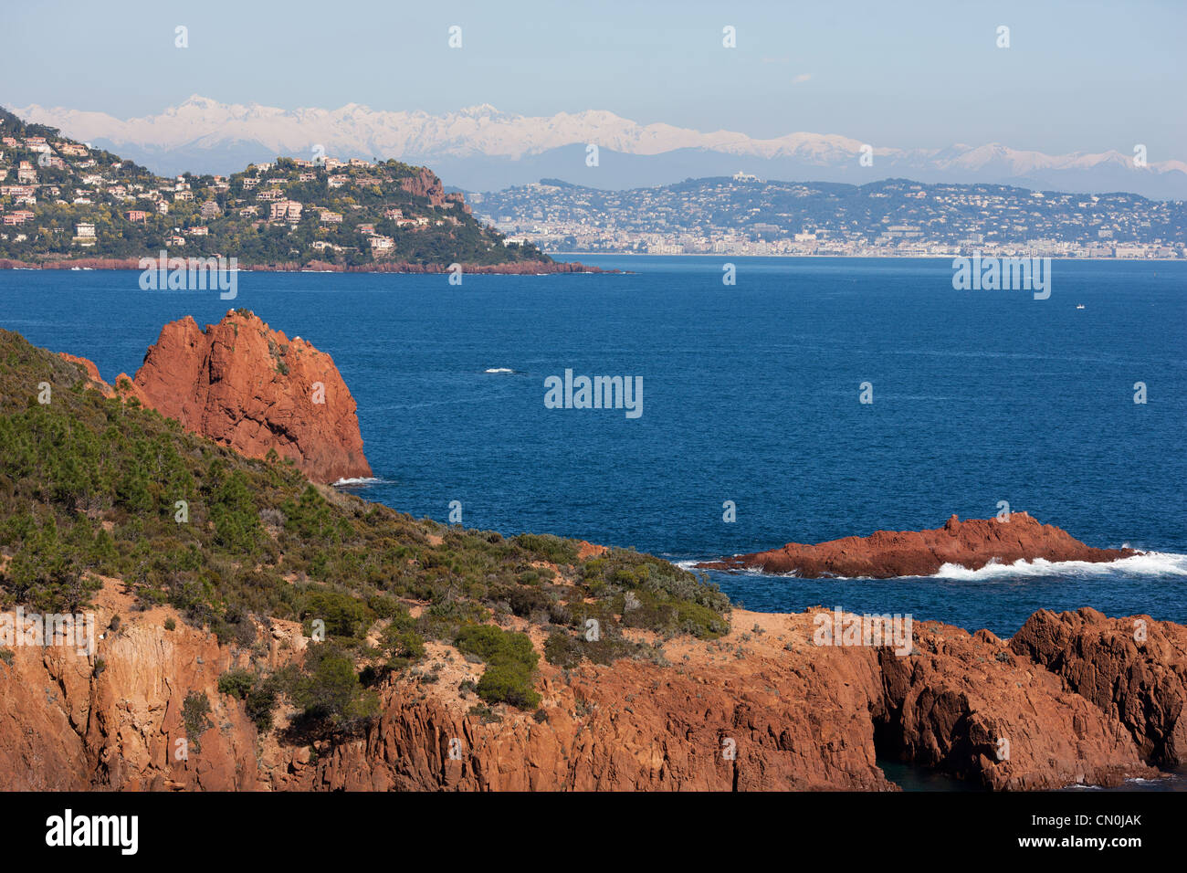 Lujosas villas en un promontorio de roca volcánica roja con Cannes y los Alpes Mercantour en la distancia. Théoule-sur-Mer, Riviera Francesa, Francia. Foto de stock
