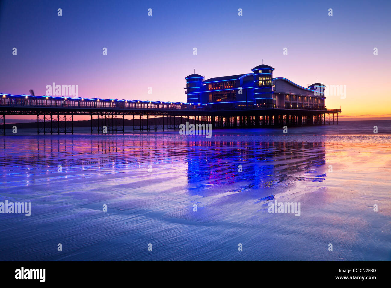 Crepúsculo sobre el Grand Pier en Weston-Super-Mare, Somerset, Inglaterra, Reino Unido refleja en la arena mojada de la playa durante la marea alta. Foto de stock