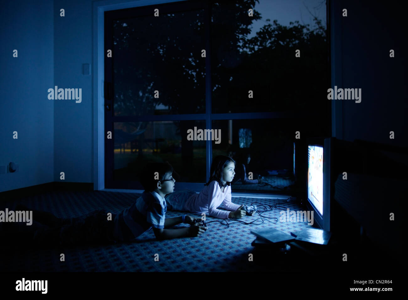 Iluminado por la pantalla, chico y chica juegan juegos de video. Foto de stock