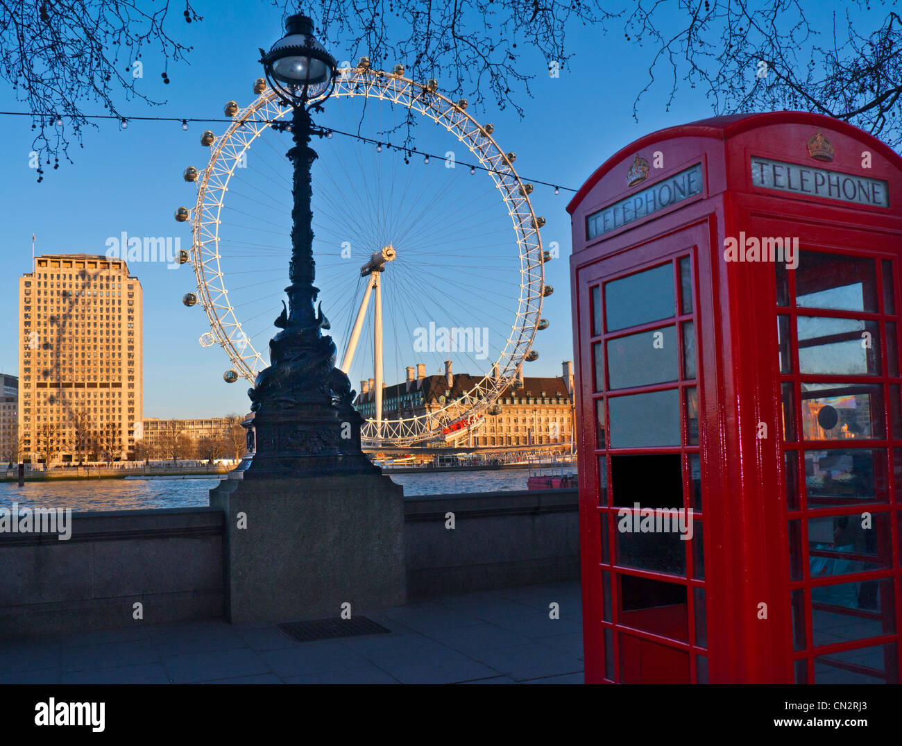 Teléfono rojo tradicional quiosco en Westminster Pier con el río Támesis y el London Eye detrás al atardecer, Londres, Gran Bretaña. Foto de stock