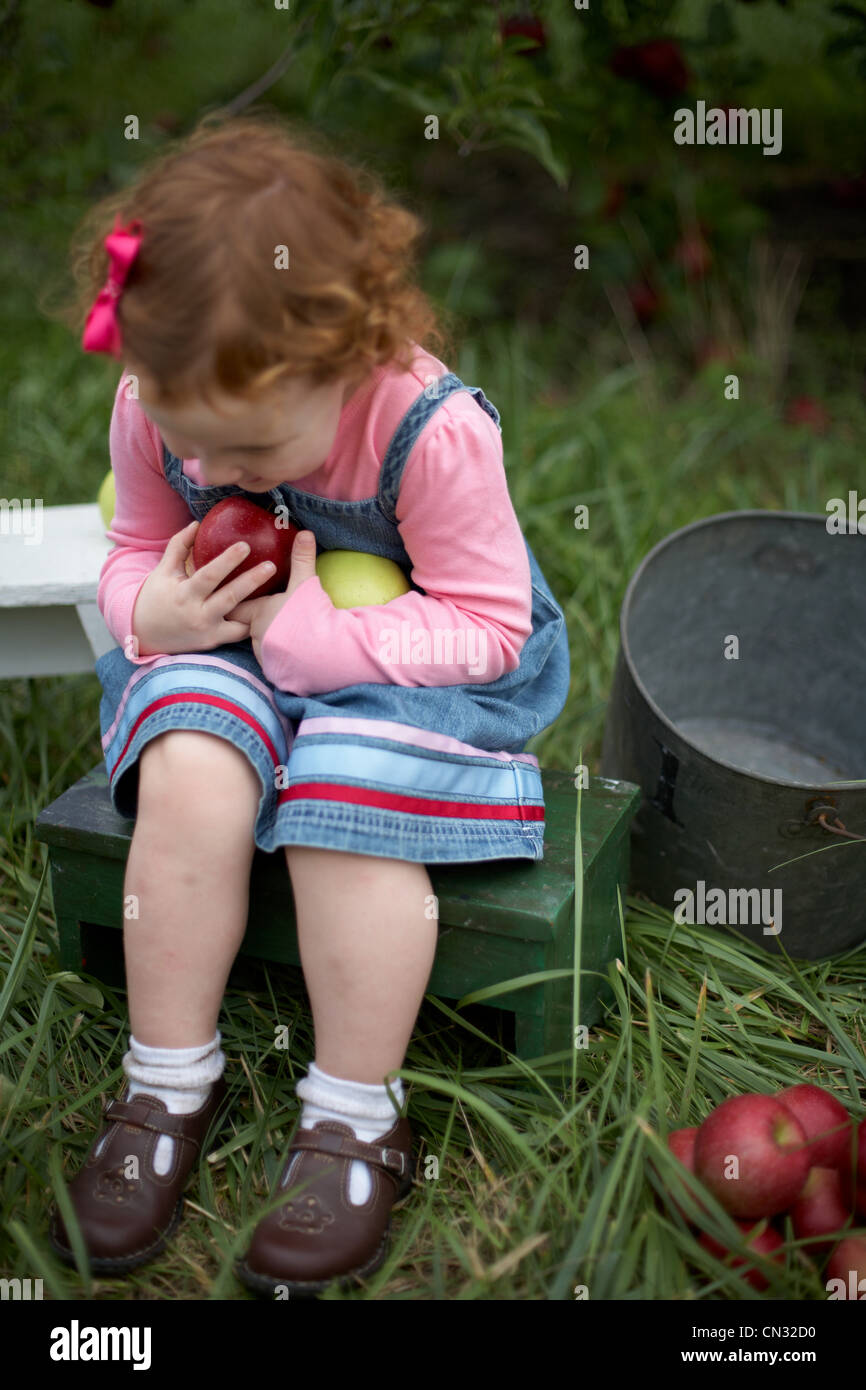 Chica sentada en un banco sosteniendo las manzanas Foto de stock