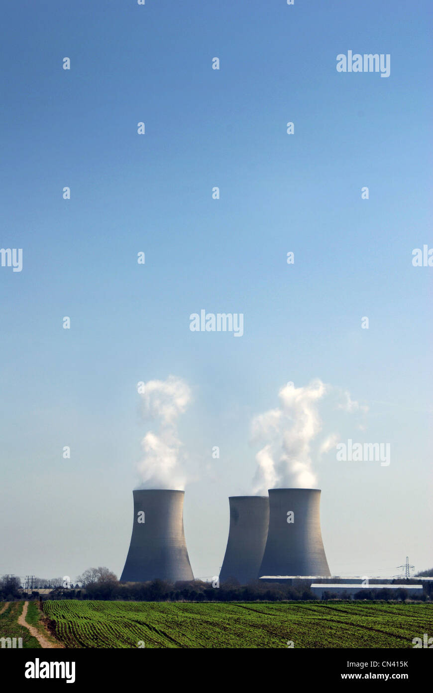 Tres torres de enfriamiento de ventilación de vapor de agua hacia el cielo azul, el campo vacío en primer plano, las plantas de energía nuclear. Foto de stock