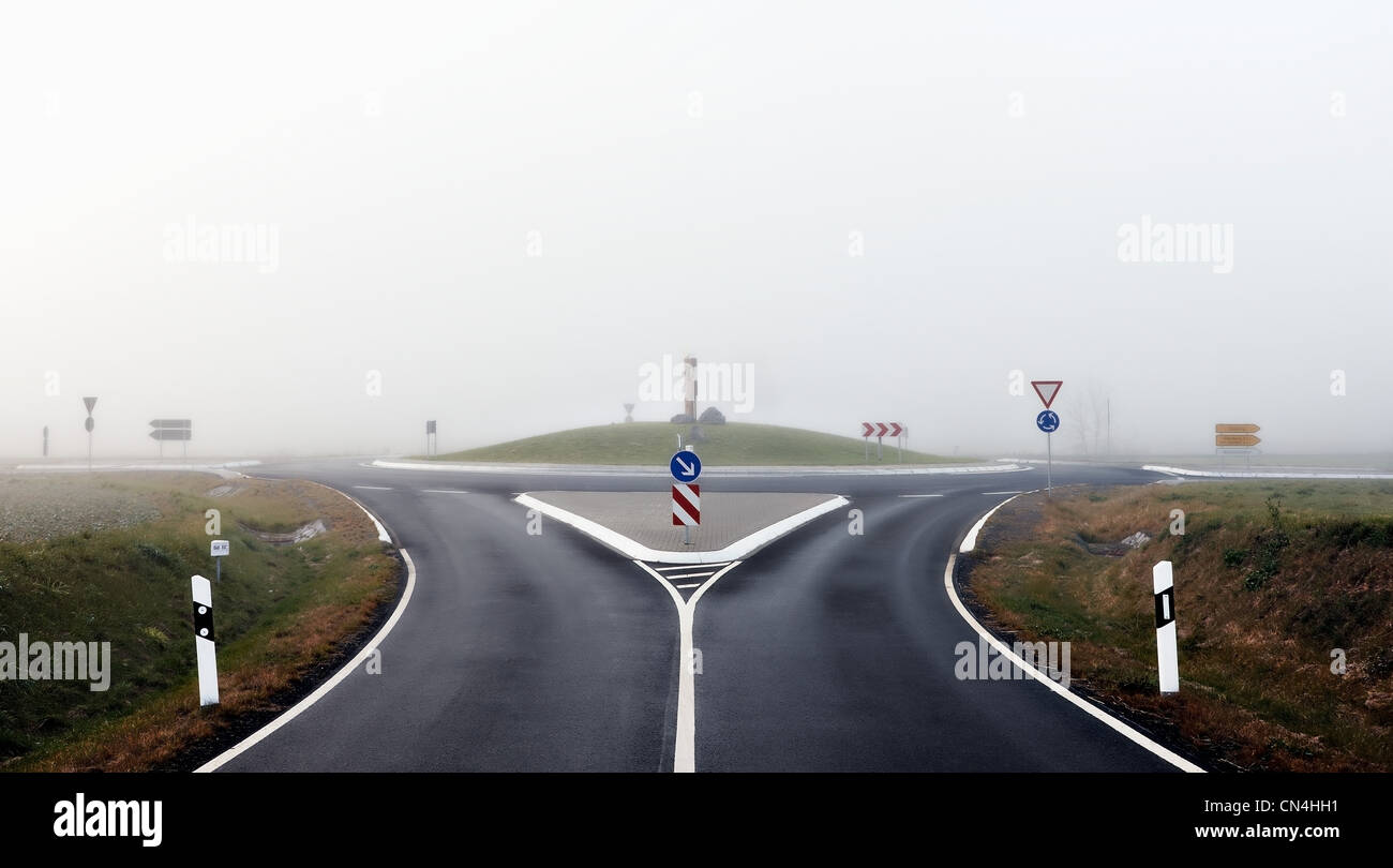 La rotonda y la carretera con señales en la niebla Foto de stock