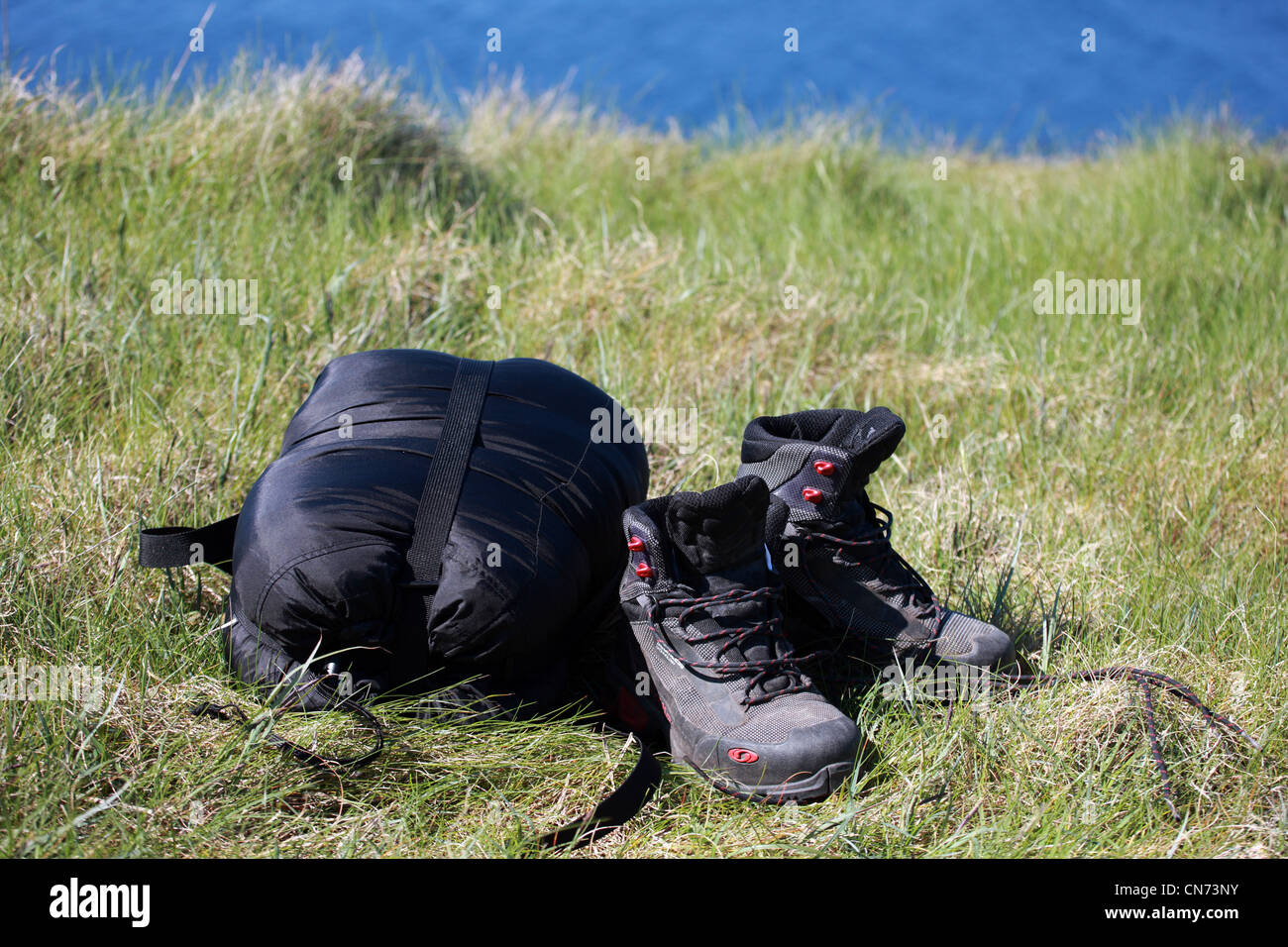 Botas de montaña y bolsa de dormir sobre la hierba junto al mar Fotografía  de stock - Alamy