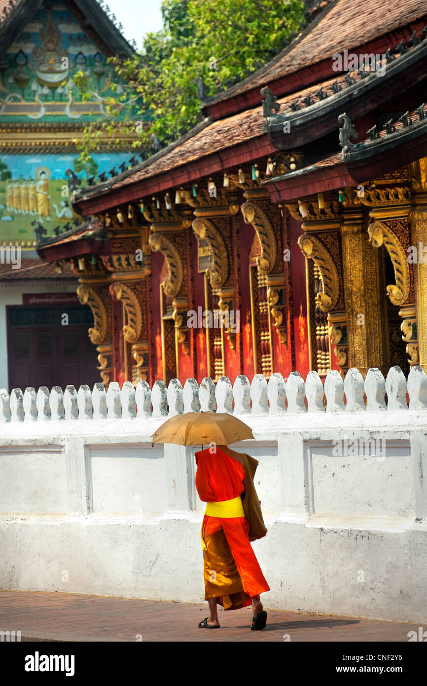 Monje con sombrilla pasaba por un templo en Luang Prabang, Laos Foto de stock