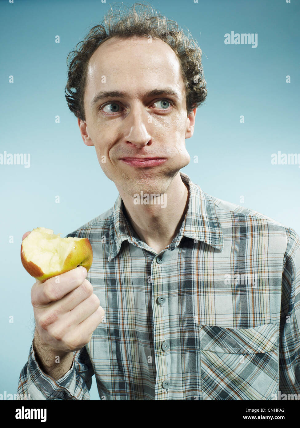 Un hombre con una mejilla abultada con un bocado de manzana, mirando hacia el lado Foto de stock