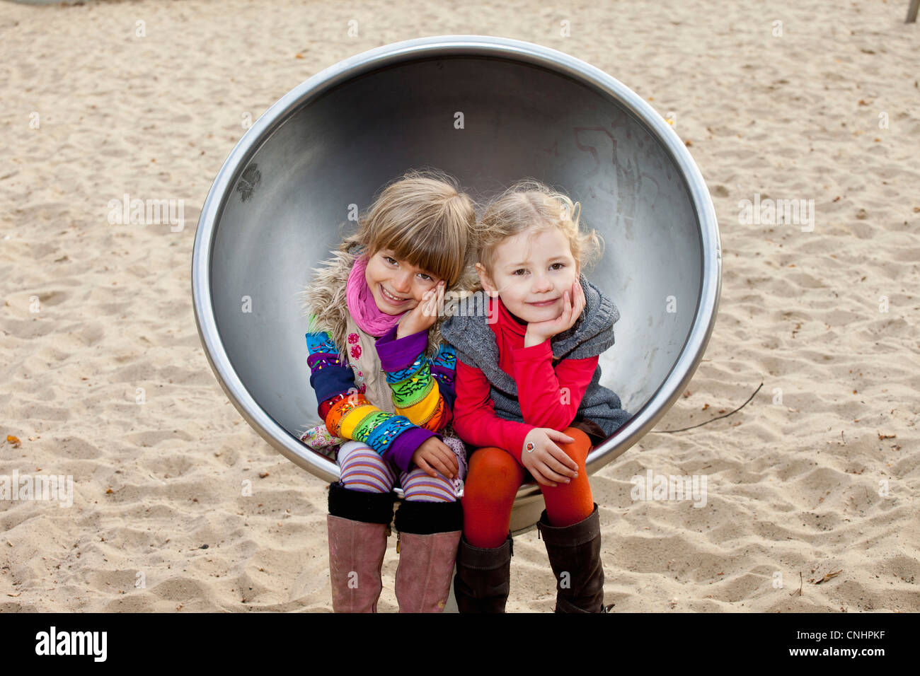 Dos niñas sentadas en silla metálica esférica en el parque Foto de stock