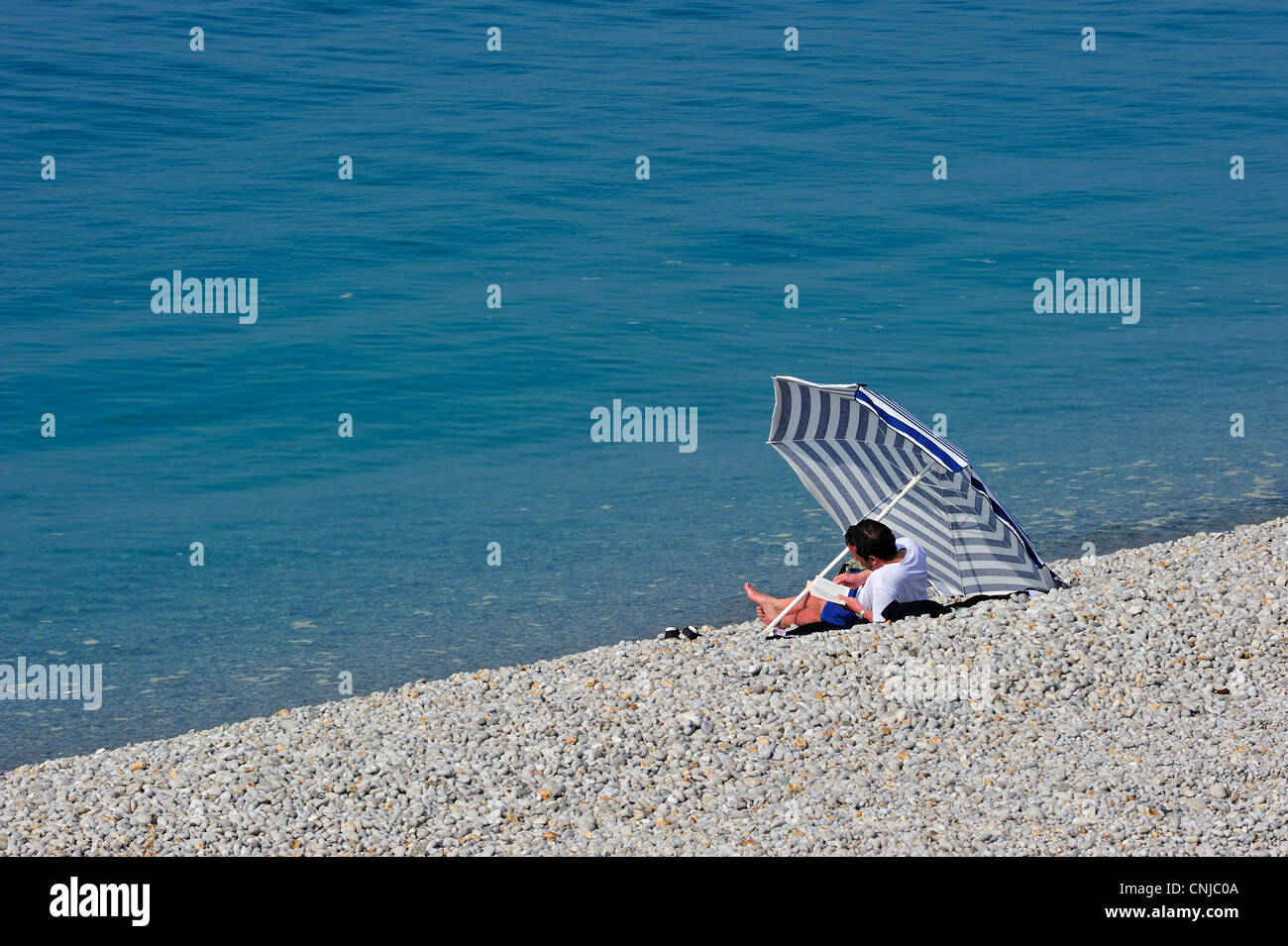 Libro de lectura turística bajo la sombrilla en la playa de guijarros en Etretat, Côte d'Albâtre, Alta Normandía, Francia Foto de stock