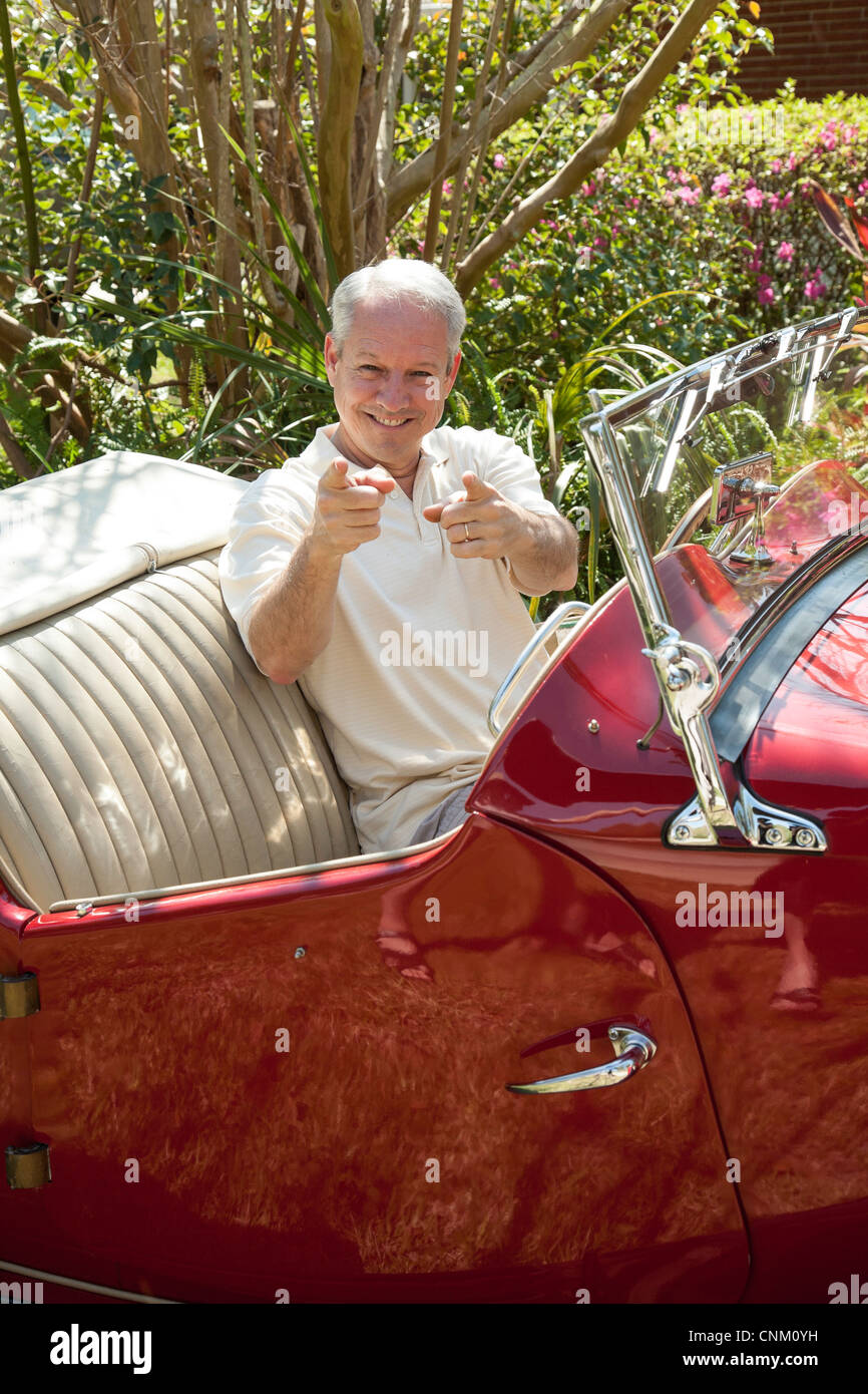 Hombre maduro, gestos de su 1953 MG vintage coche deportivo convertible. Foto de stock