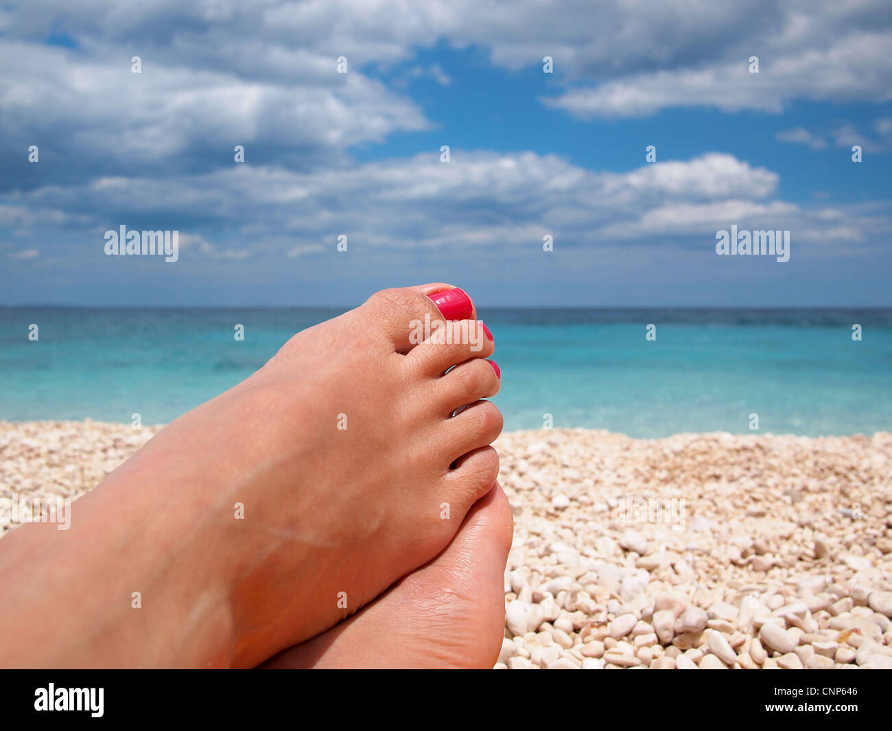 Los pies femeninos con clavos pulidos rojo perezoso relajante en la playa. Foto de stock