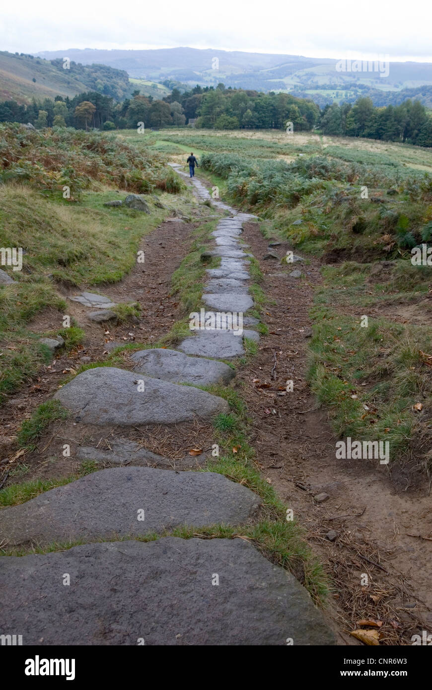 Diminuta figura caminando en el sendero de piedra de granito procedente de Stanage Borde oscuro, Derbyshire Peak, Peak District, REINO UNIDO Foto de stock